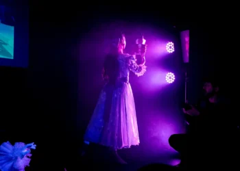 Cena teatral iluminada por luz roxa durante apresentação do Programa de Qualificação em Artes