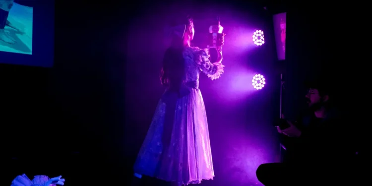 Cena teatral iluminada por luz roxa durante apresentação do Programa de Qualificação em Artes