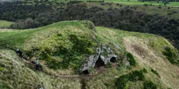 Entrada de caverna cercada por vegetação, imagem ilustrativa para matéria sobre trilhas e cavernas em parque nacional